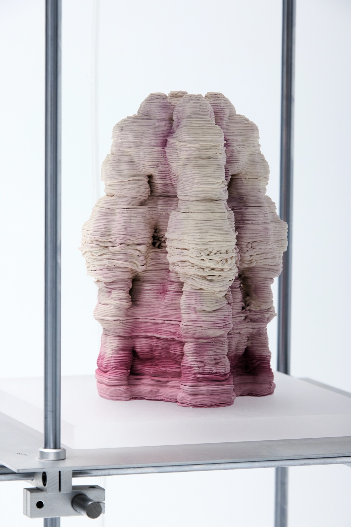 Close view of one piece on its plinth: thick printed coils running white to deep pink, the layered surface catching the pigment unevenly.